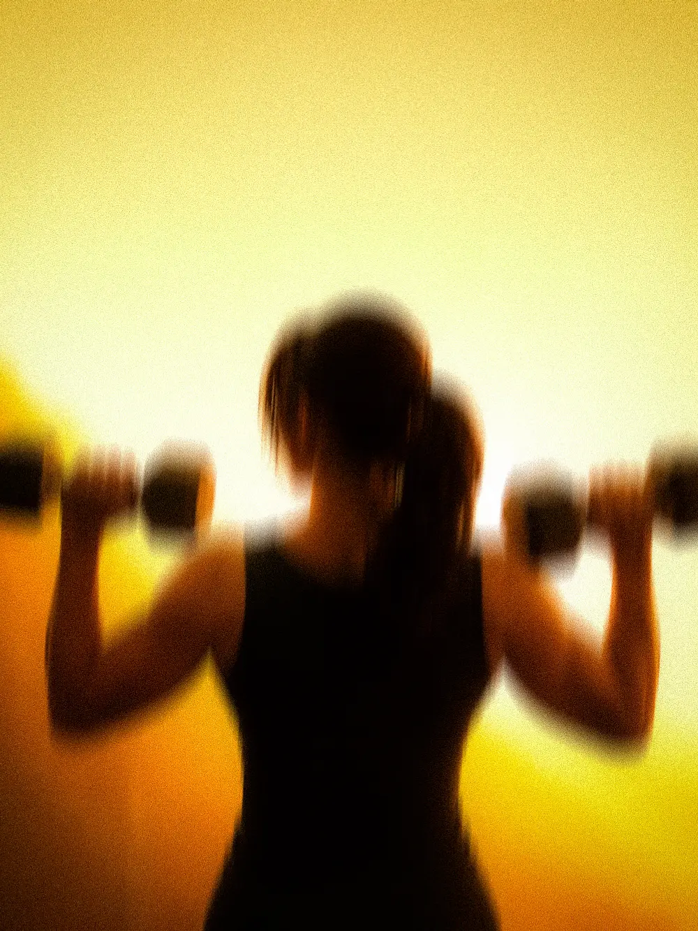A member pressing dumbbells overhead in the amber light of ASAI GYM