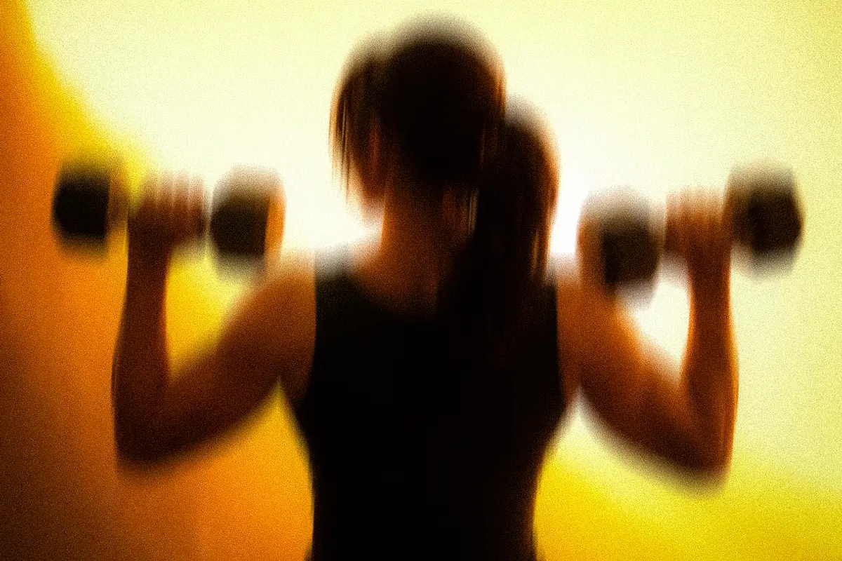 A member pressing dumbbells overhead, silhouetted against morning amber light