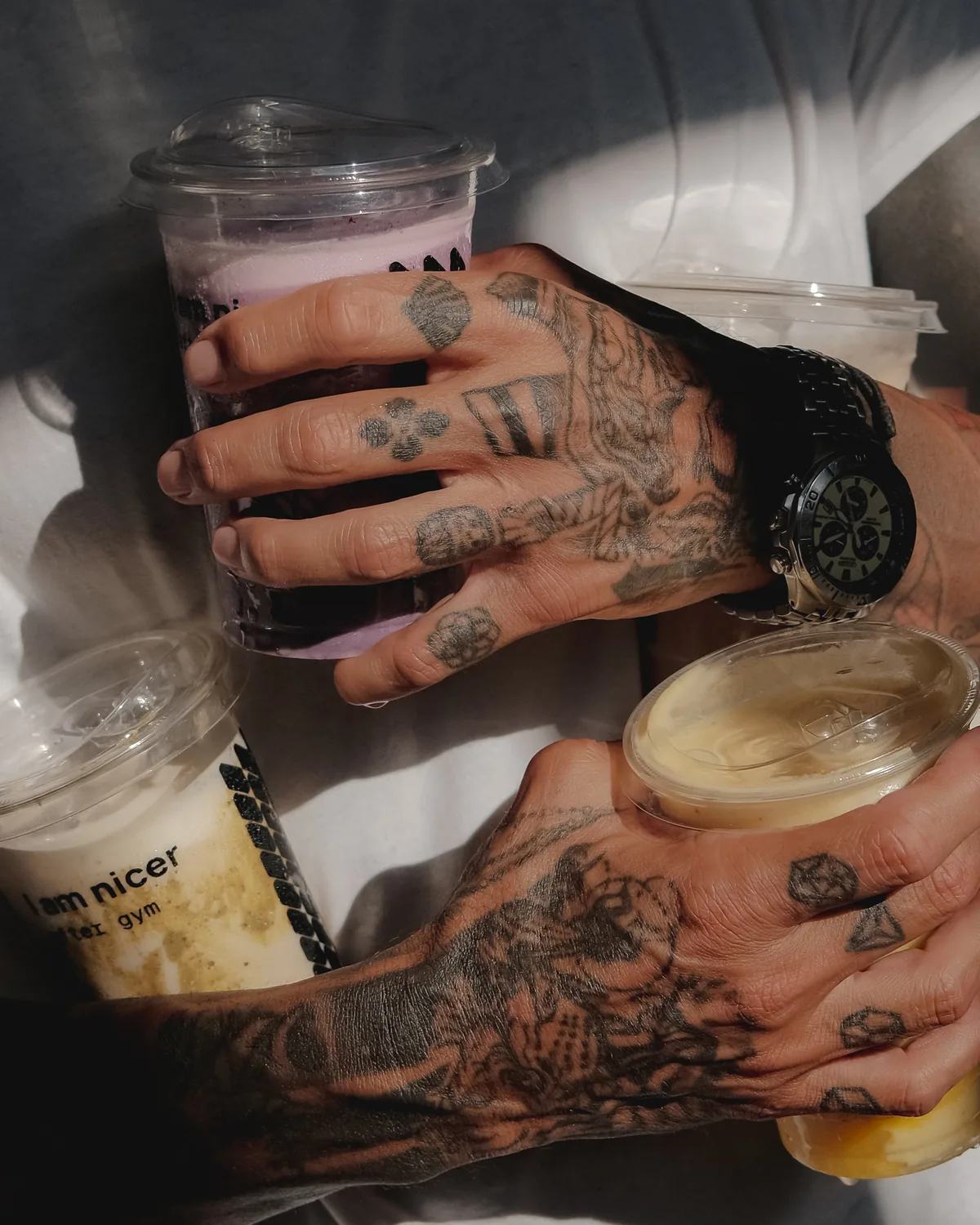 Tattooed hands holding three ASAI GYM smoothies in branded cups